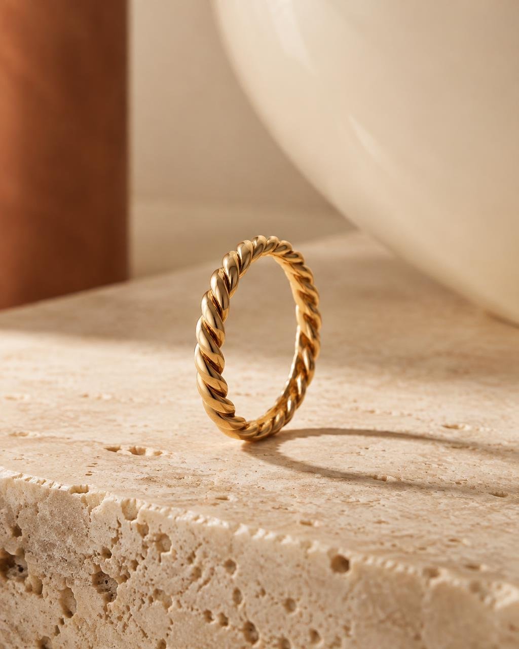 Twisted yellow gold rope ring on pale travertine